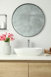 Photo of Vase with beautiful pink tulips and toiletries near sink in bathroom