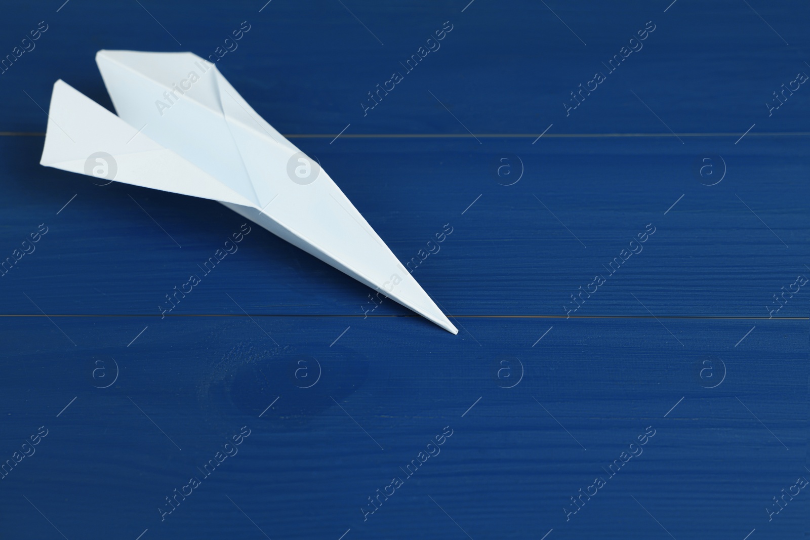 Photo of Handmade paper plane on blue wooden table, closeup. Space for text