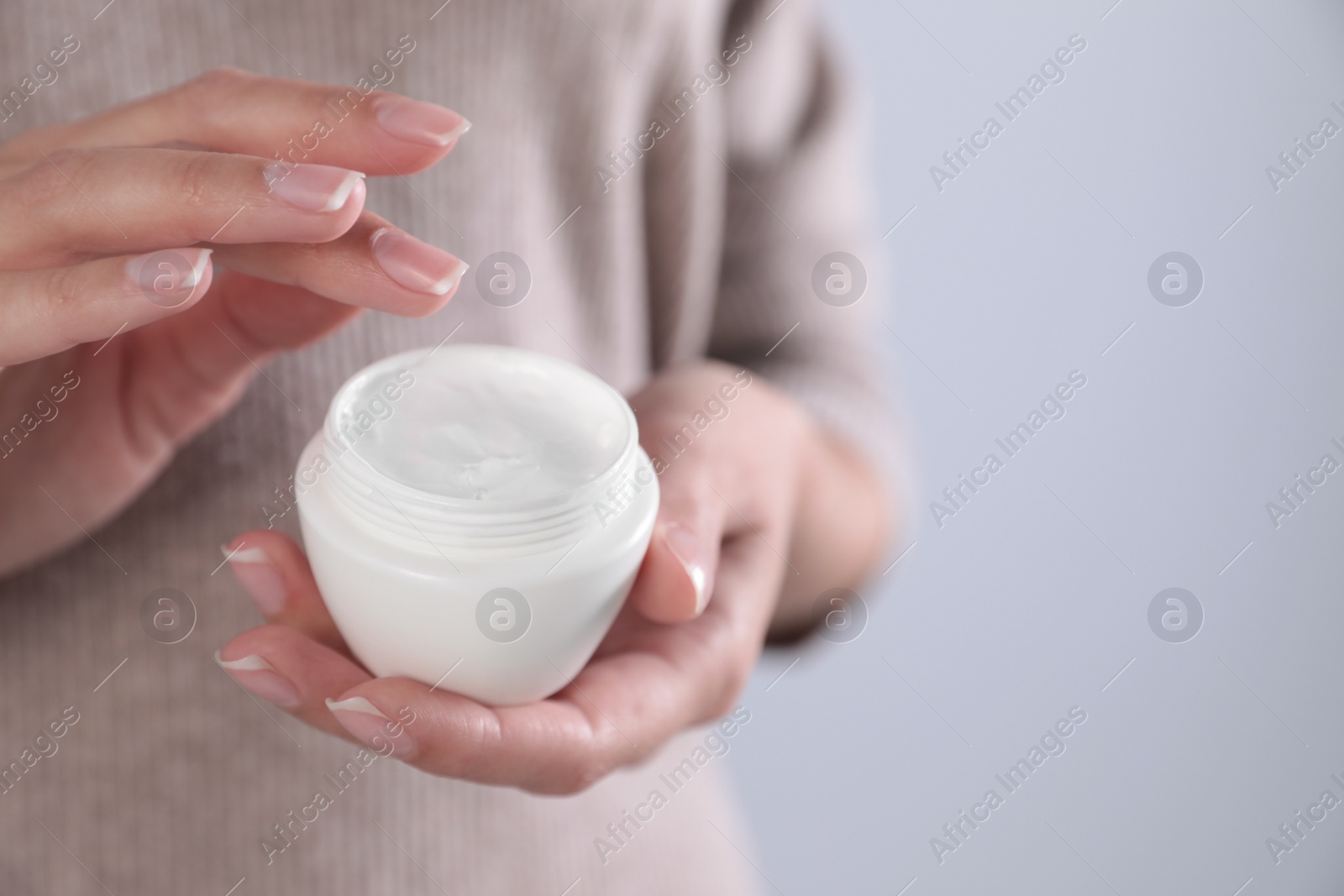 Photo of Young woman holding jar of cream on grey background, closeup. Space for text