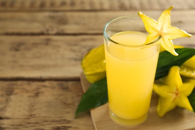 Delicious carambola juice in glass on wooden table. Space for text