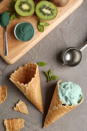 Photo of Flat lay composition with delicious spirulina ice cream cones and scoop on grey background
