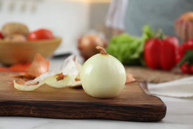 Photo of Wooden board with fresh onion and peels on white marble table, closeup