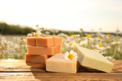 Photo of Chamomile soap bars on wooden table in field