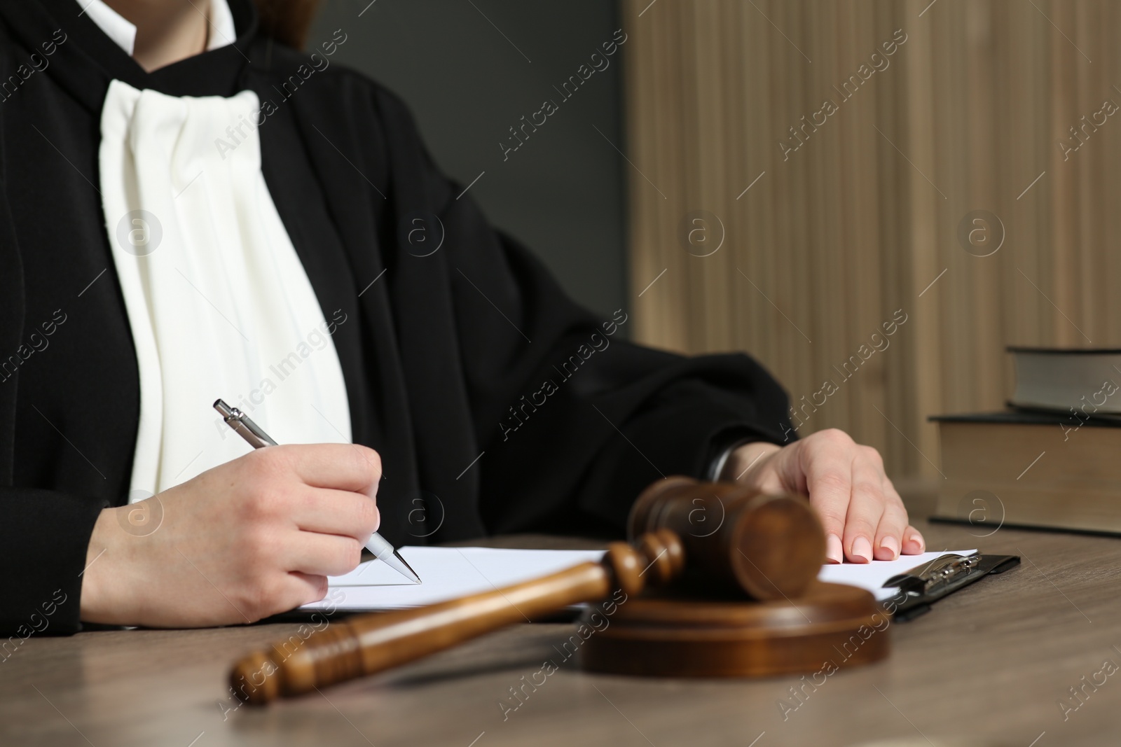 Photo of Judge with pen and clipboard working at wooden table in courtroom, closeup