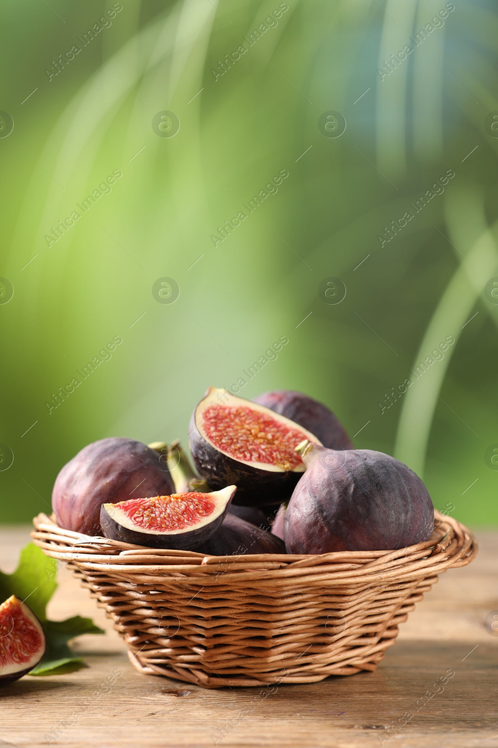 Photo of Wicker bowl with fresh ripe figs on wooden table. Space for text