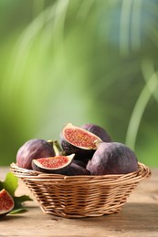 Wicker bowl with fresh ripe figs on wooden table. Space for text