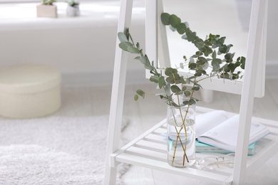 Photo of Vase with fresh eucalyptus branches on mirror shelf in room. Interior design