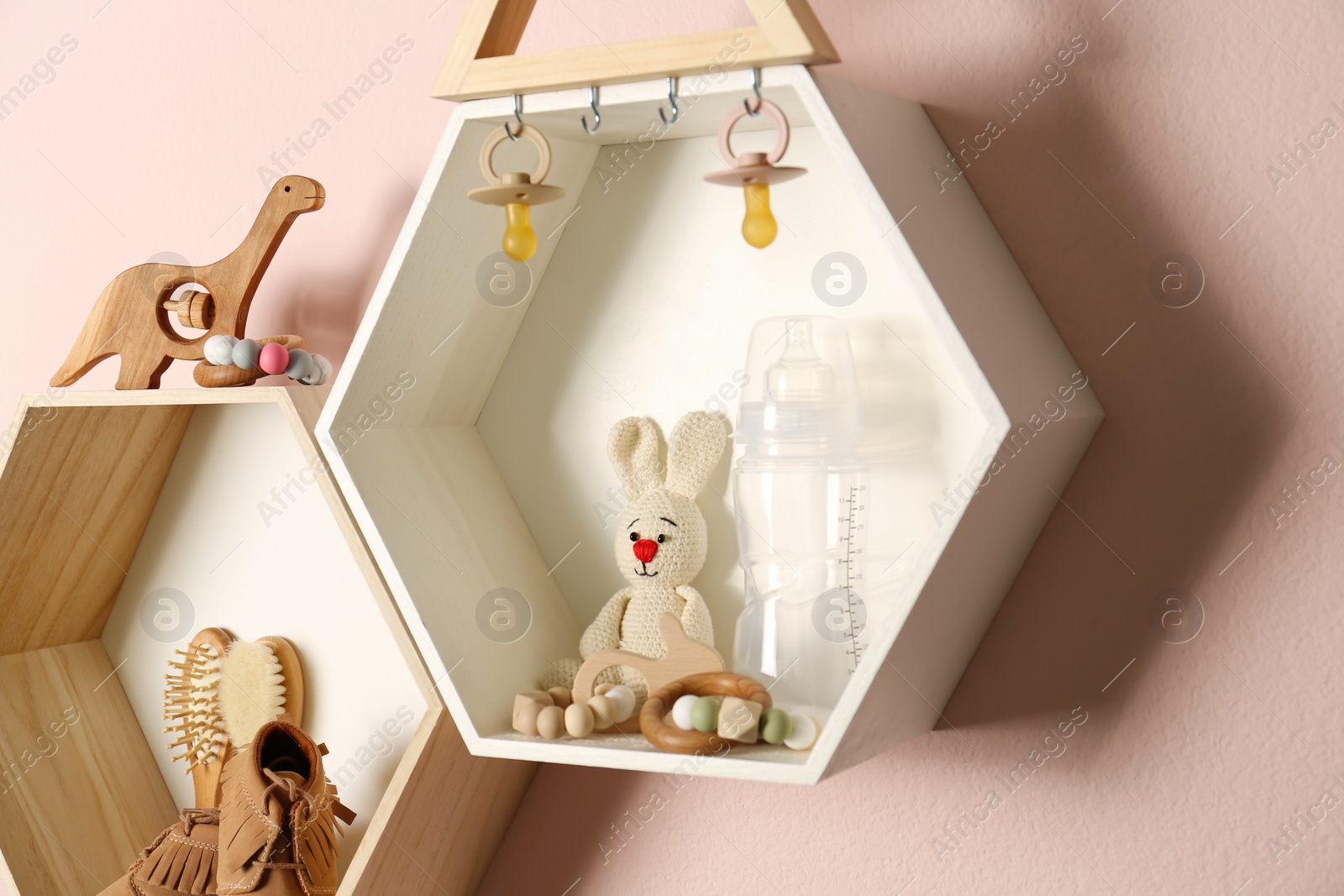 Photo of Hexagon shaped shelves with toys and child's accessories on pink wall. Interior design