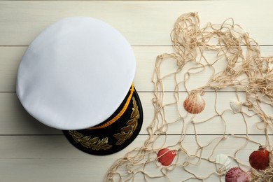 Photo of Peaked cap, net and shells on white wooden background, flat lay