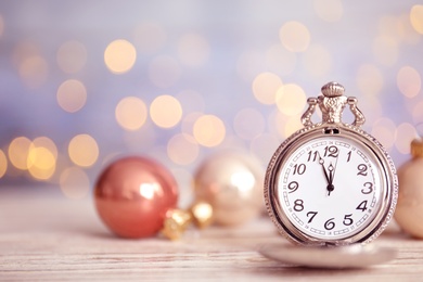 Photo of Pocket watch and festive decor on table against blurred lights, space for text. New Year countdown