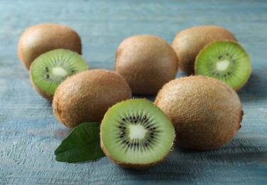 Photo of Cut and whole fresh ripe kiwis on light blue wooden table, closeup