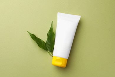 Tube of face cream and fresh leaves on light green background, flat lay