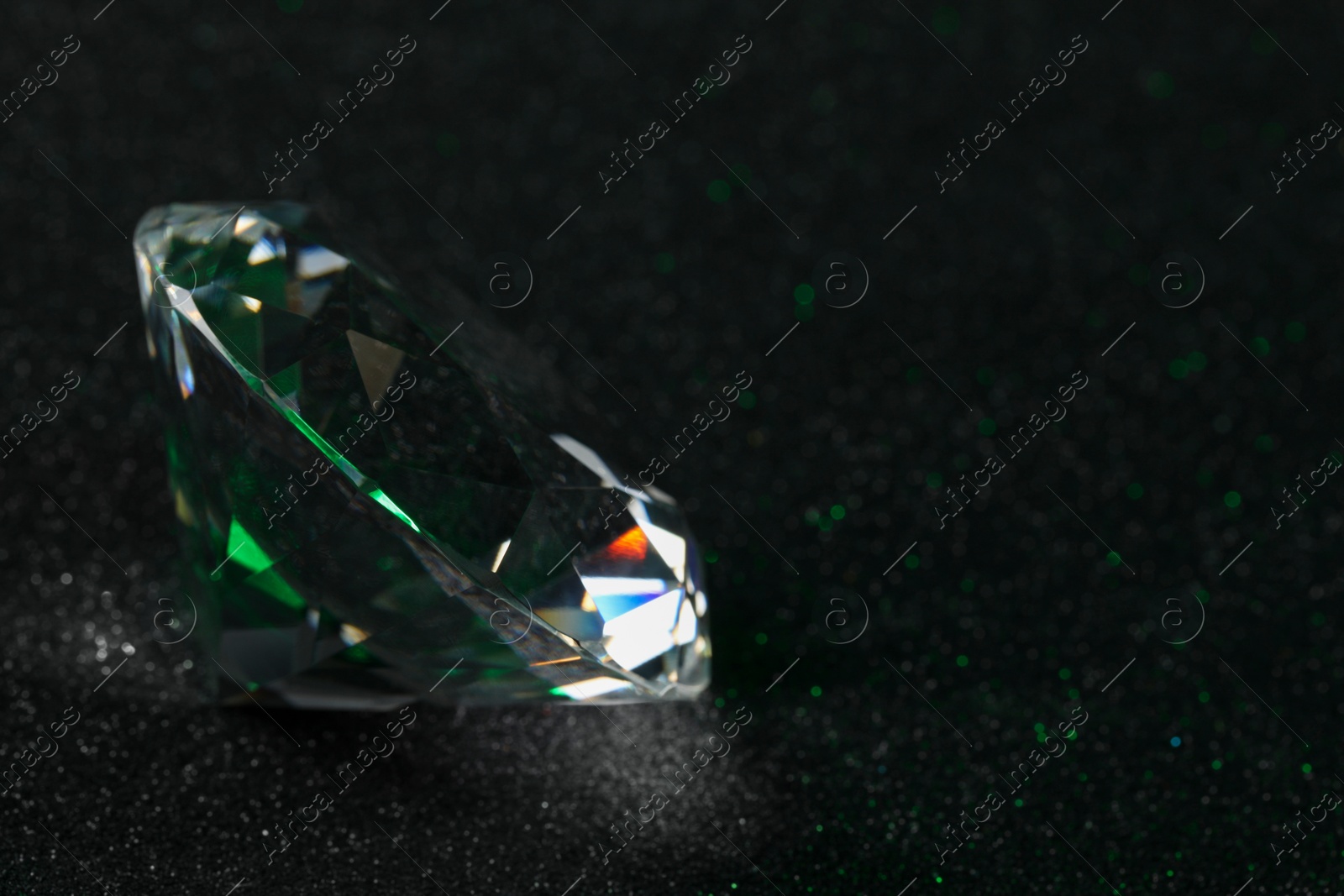 Photo of Beautiful dazzling diamond on dark glitter surface, closeup. Space for text