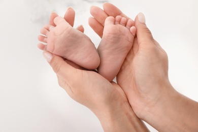 Mother holding baby's feet on light background, closeup