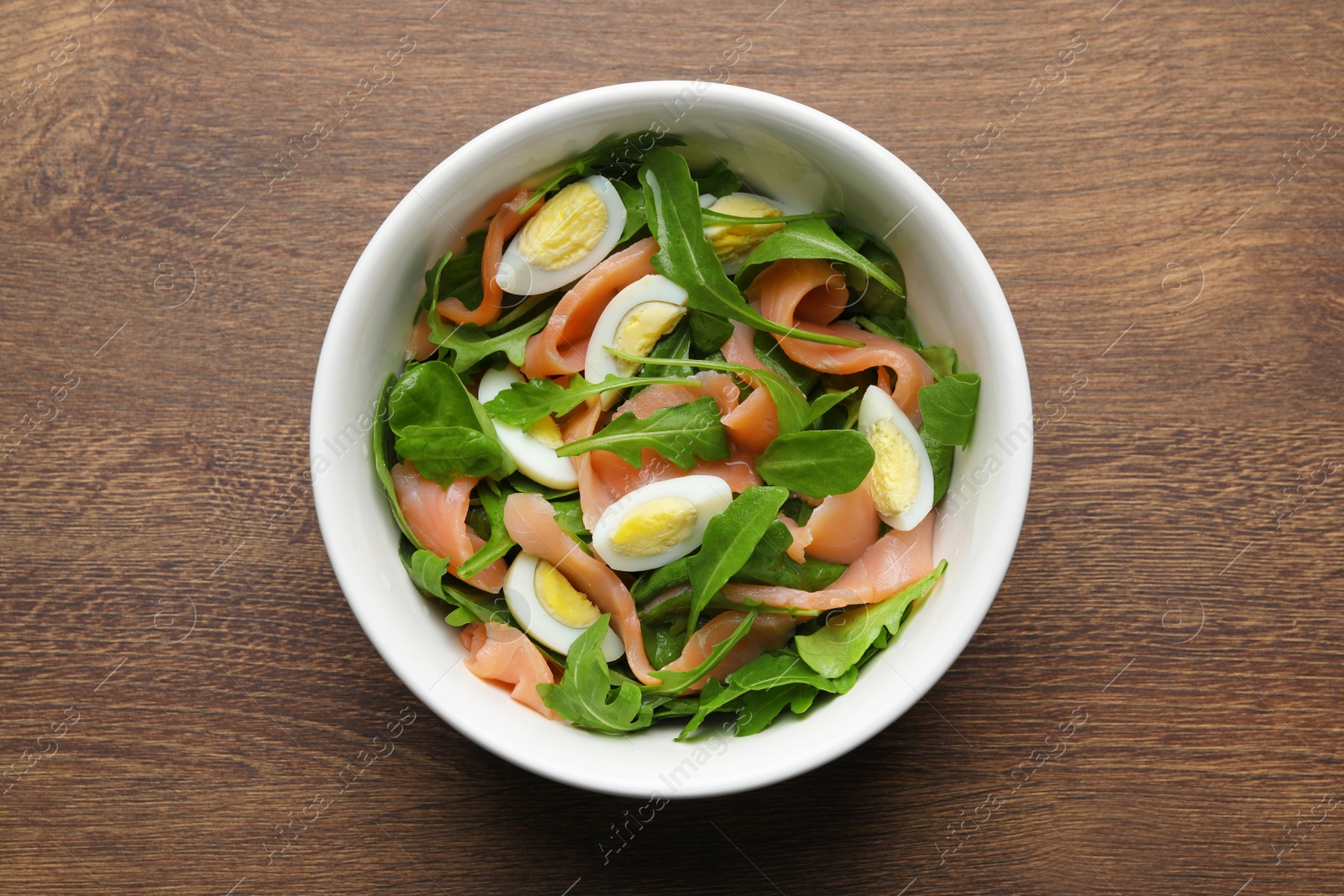 Photo of Delicious salad with boiled eggs, salmon and arugula on wooden table, top view