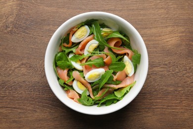 Photo of Delicious salad with boiled eggs, salmon and arugula on wooden table, top view