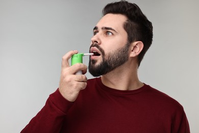 Young man using throat spray on grey background