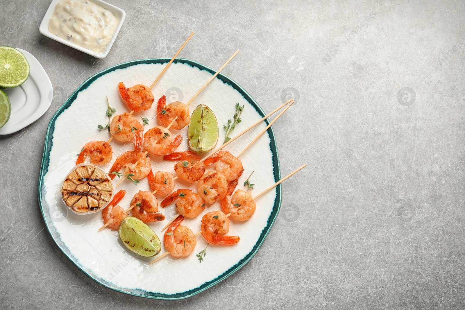 Photo of Plate with delicious fried shrimp skewers and lime on grey background, top view