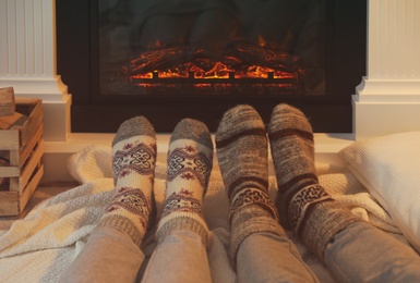 Couple in warm socks resting near fireplace at home, closeup