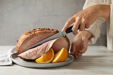 Woman cutting delicious baked ham at white wooden table, closeup