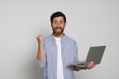 Photo of Happy handsome man with laptop on light background