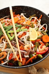 Shrimp stir fry with noodles and vegetables in wok on table, closeup