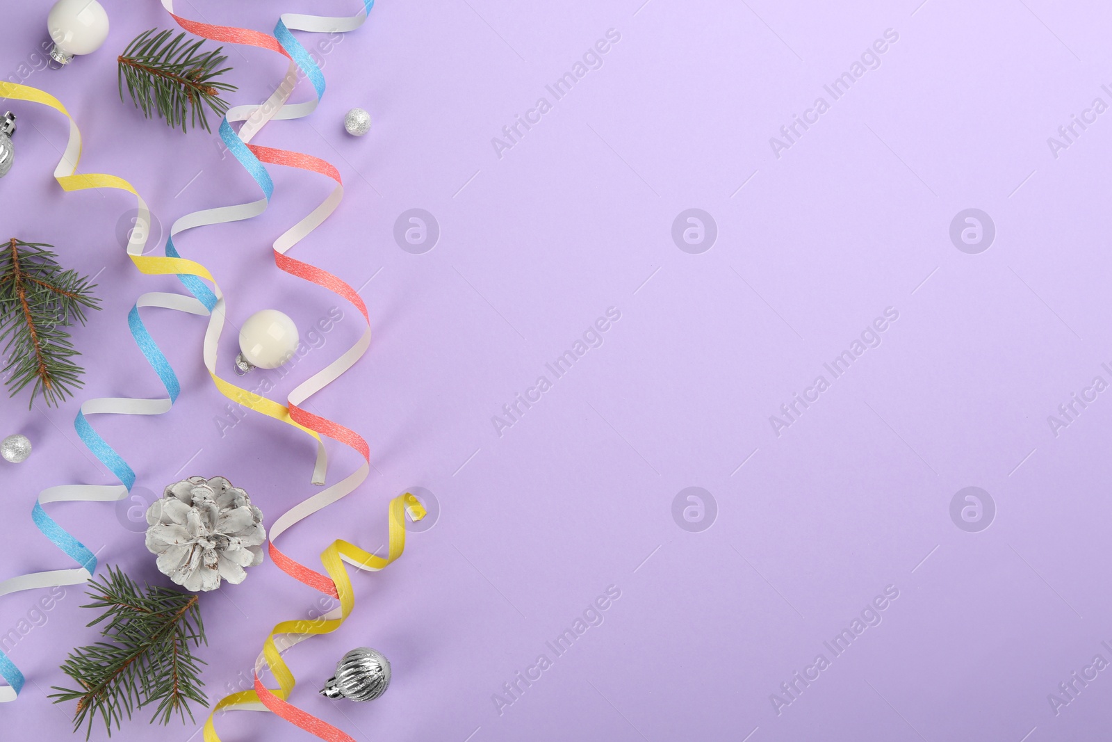 Photo of Colorful serpentine streamers, Christmas balls and fir branches on violet background, flat lay. Space for text