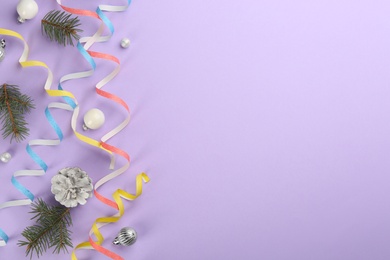 Colorful serpentine streamers, Christmas balls and fir branches on violet background, flat lay. Space for text