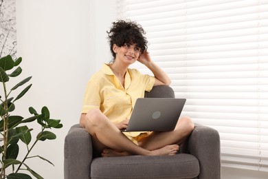 Photo of Beautiful young woman in stylish pyjama with laptop on armchair at home