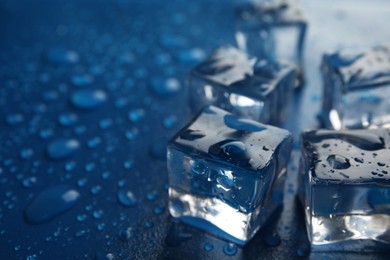 Photo of Ice cubes with water drops on blue background, closeup. Space for text