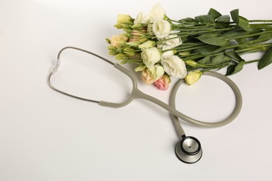 Photo of Stethoscope and eustoma flowers on white background, above view. Happy Doctor's Day