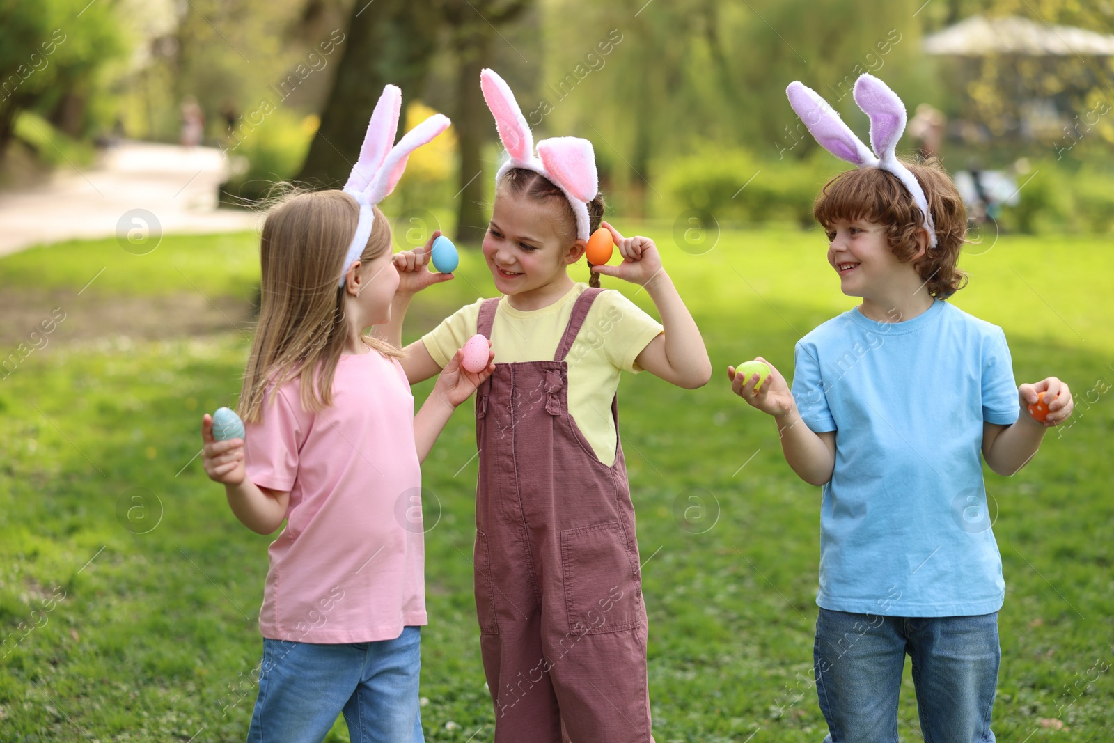 Photo of Easter celebration. Cute little children in bunny ears holding painted eggs outdoors