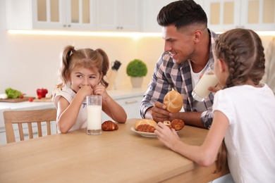 Photo of Little girls and their father eating together at table in modern kitchen