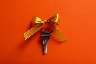 Photo of Key with yellow bow on orange background, top view. Housewarming party