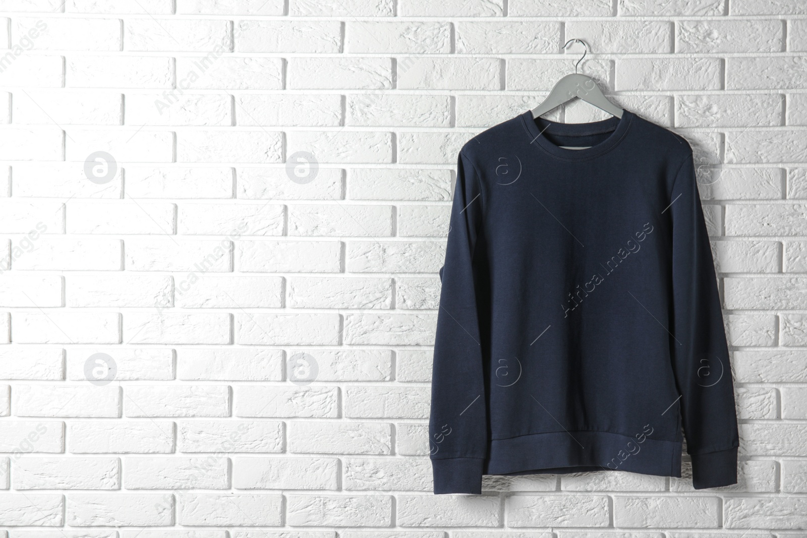 Photo of Hanger with dark sweatshirt against brick wall. Mockup for design