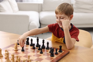 Photo of Little boy playing chess at table in room