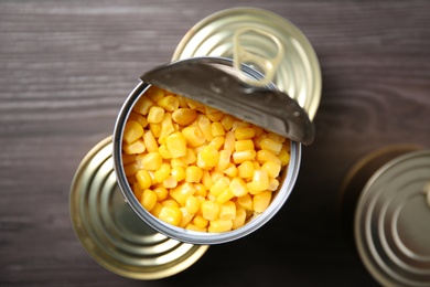 Open tin can of sweet corn and conserves on wooden table, top view