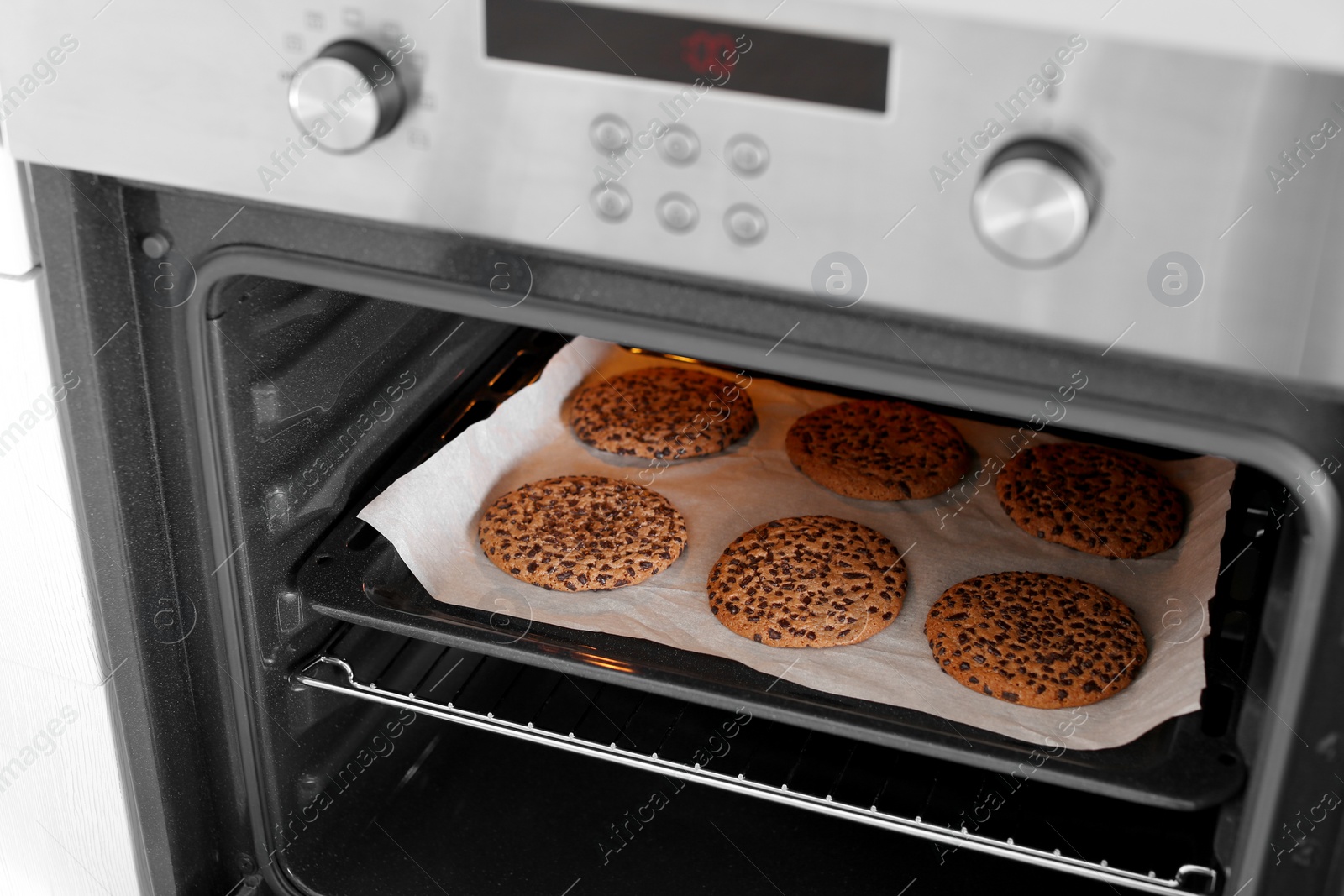 Photo of Open modern oven with freshly baked cookies on sheet in kitchen