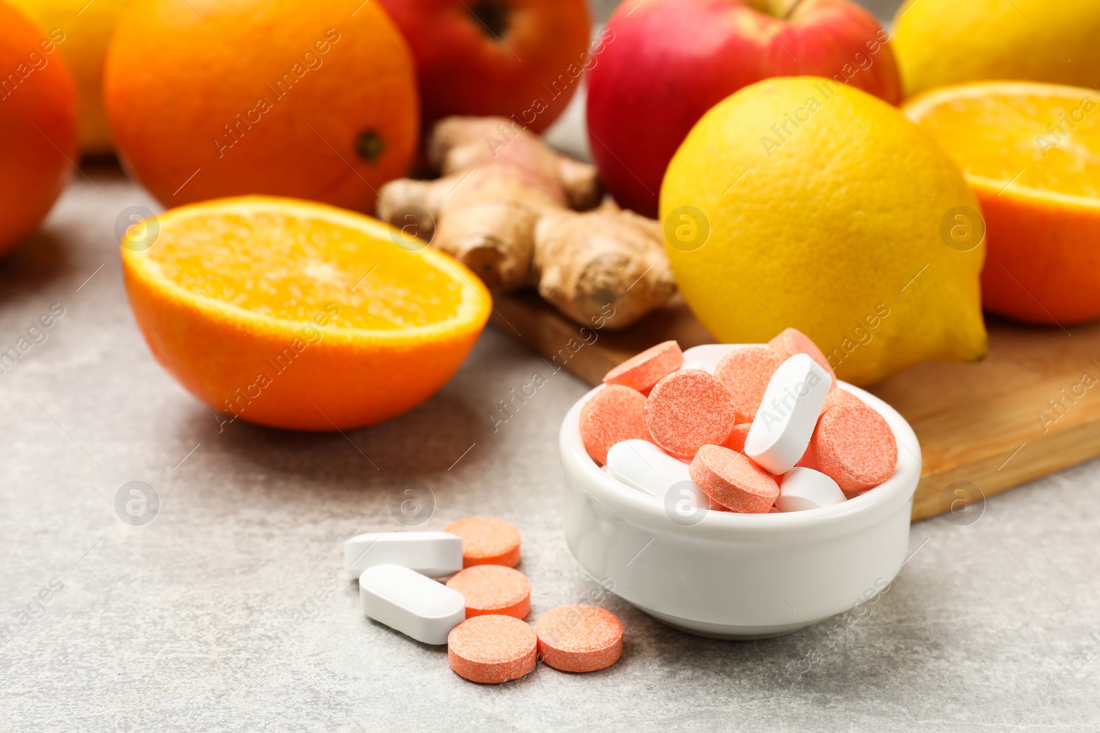 Photo of Dietary supplements. Different pills in bowl, fruits and ginger on grey table