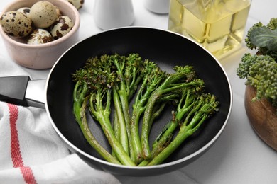 Photo of Frying pan with tasty cooked broccolini and other different products on white table, closeup