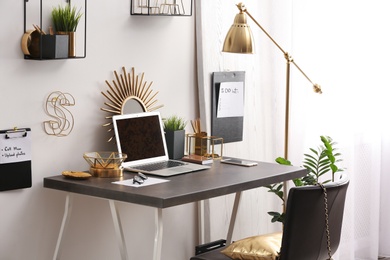 Modern workplace with laptop and golden decor on desk near wall. Stylish interior design