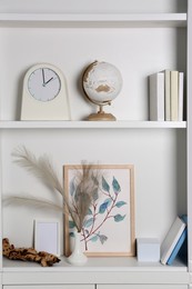 Photo of White shelves with books, globe and different decor indoors. Interior design