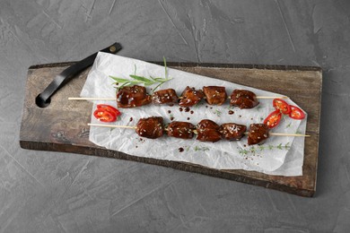 Skewers with pieces of tasty chicken meat glazed in soy sauce, herbs and cut chili pepper on grey textured table, top view
