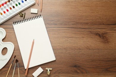 Flat lay composition with sketchbook and drawing tools on wooden table, space for text