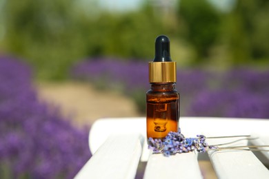 Photo of Bottle of essential oil and lavender flowers on white wooden table in field, closeup