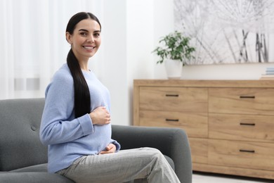 Photo of Happy pregnant woman on sofa at home, space for text