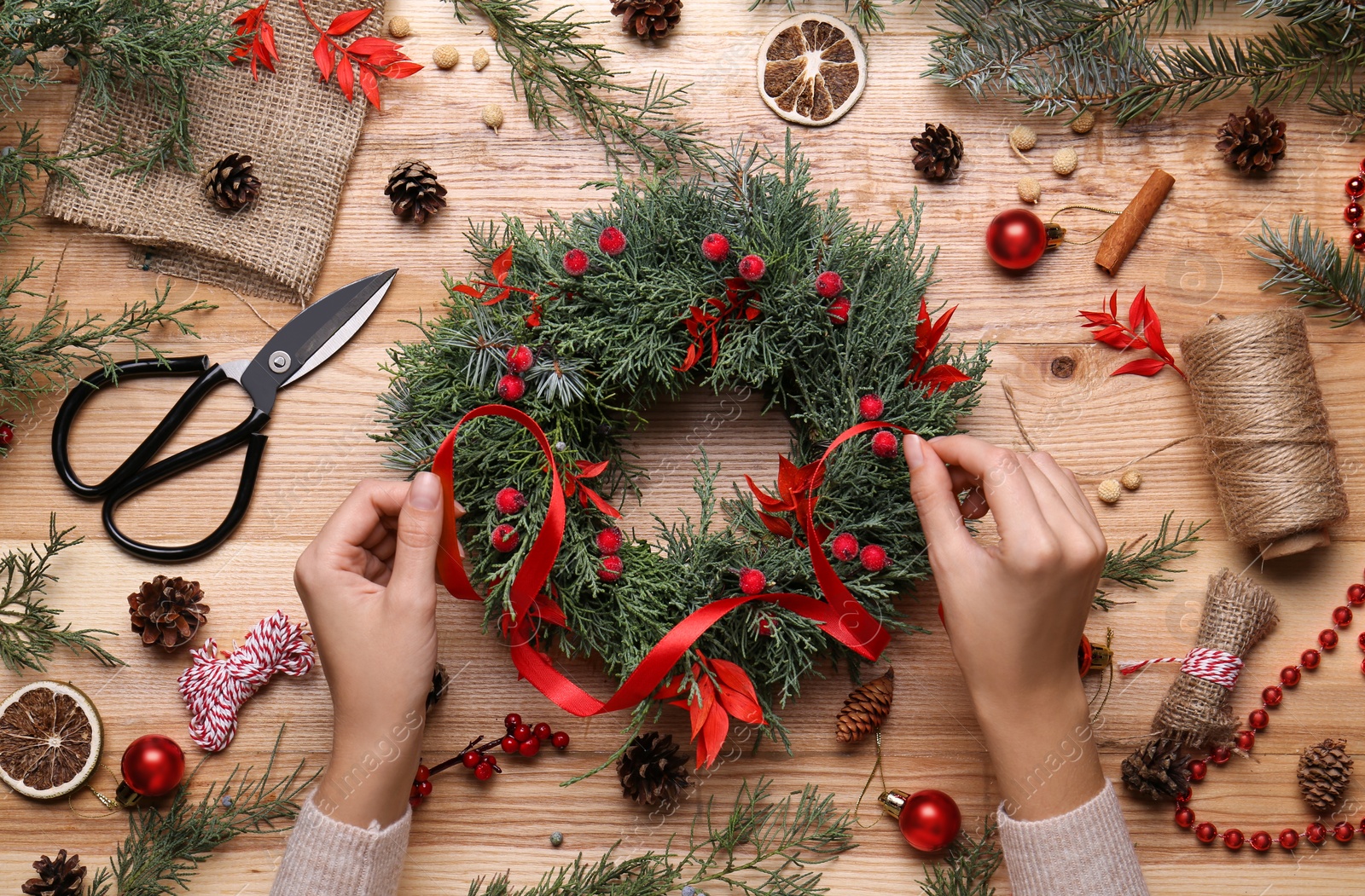 Photo of Florist making beautiful Christmas wreath with berries and red ribbon at wooden table, top view