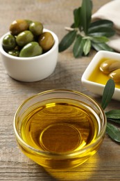 Photo of Fresh oil, ripe olives and green leaves on wooden table