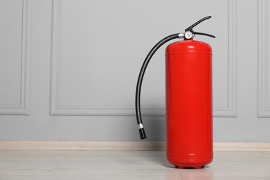 Red fire extinguisher near grey wall, space for text