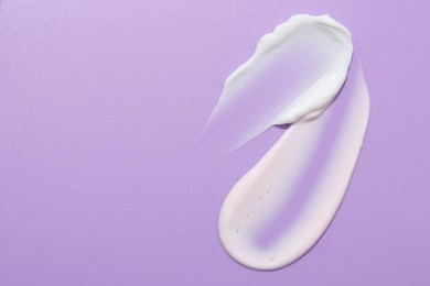 Photo of Samples of face cream on violet background, top view. Space for text